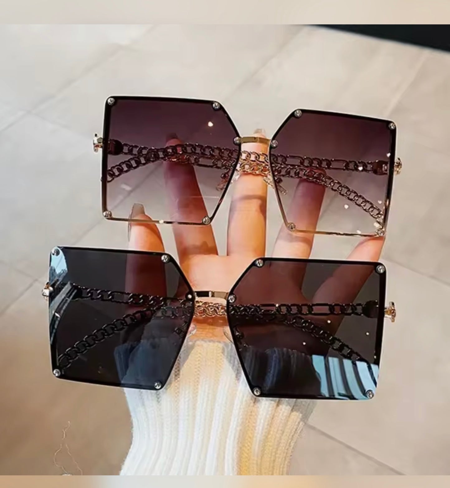 GrayBlack and Black sunglasses with chain details held by a hand on a light background  