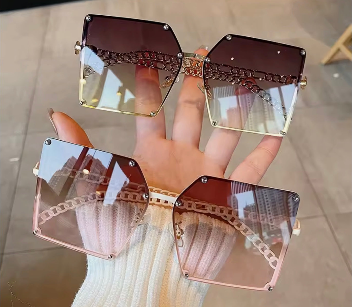 Green and White Sunglasses with a gold chain design held by a hand on a tiled floor. 