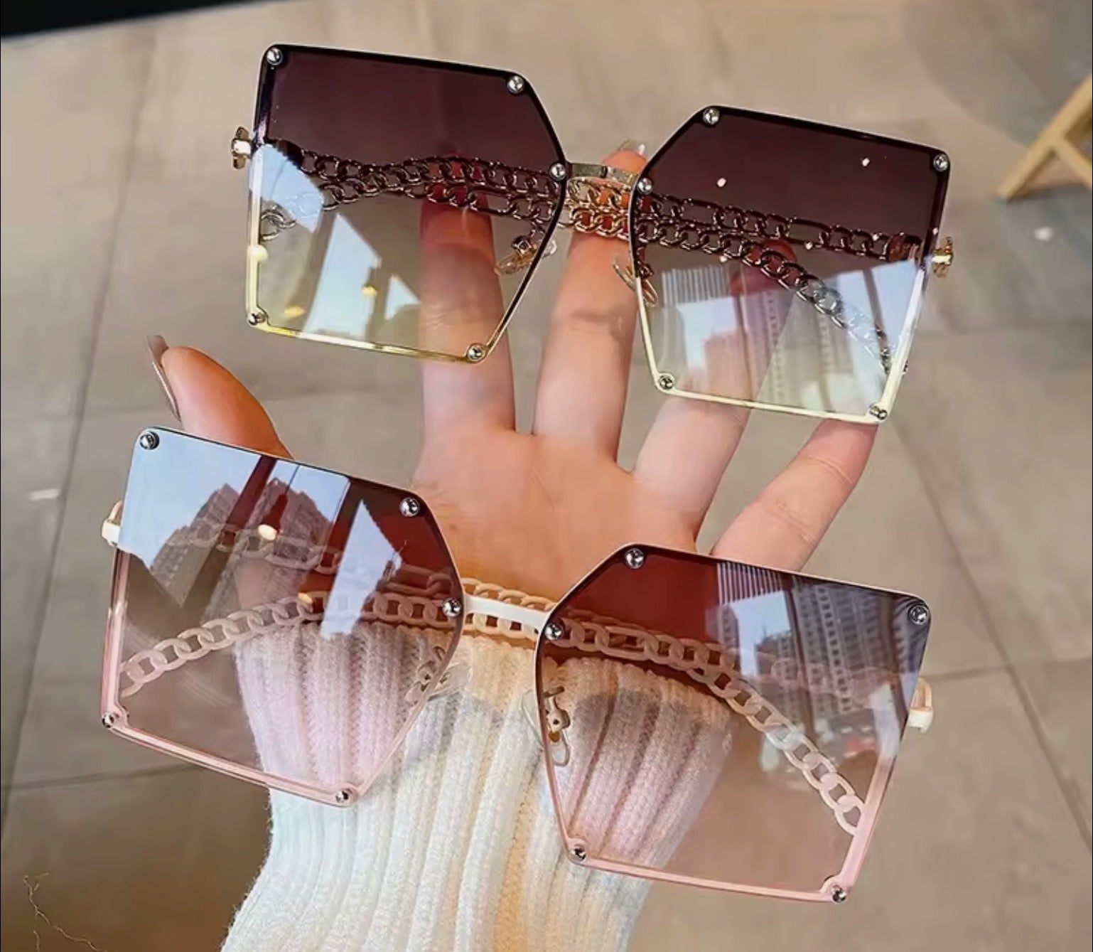 Green and White Sunglasses with a gold chain design held by a hand on a tiled floor. 