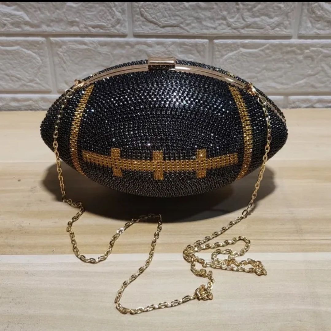 A black and gold rhinestone clutch bag designed in the shape of a football, with a golden chain handle.