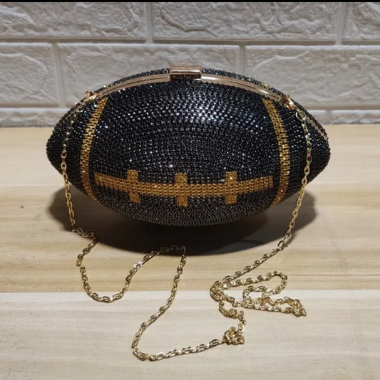 A black and gold rhinestone clutch bag designed in the shape of a football, with a golden chain handle.