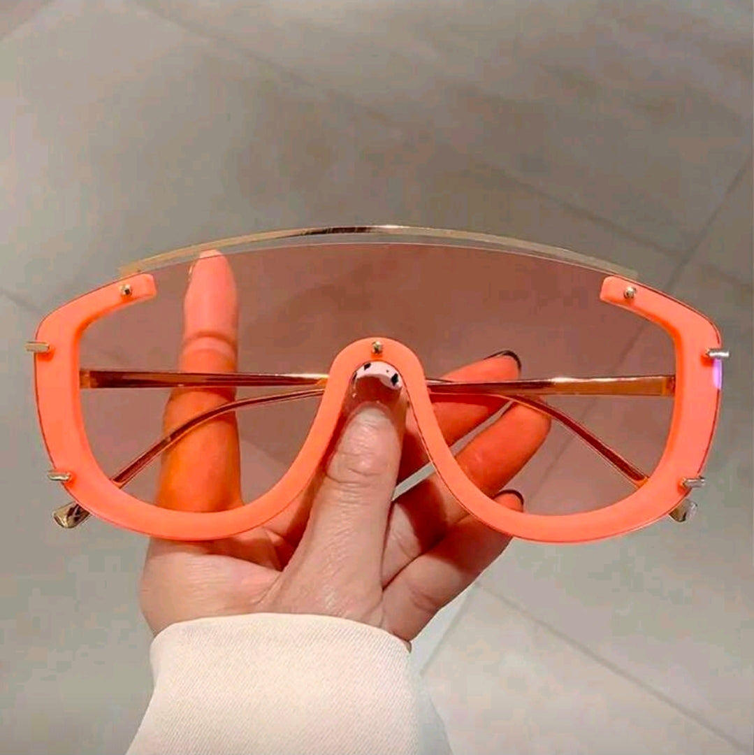 Hand holding orange sunglasses with a neutral background
